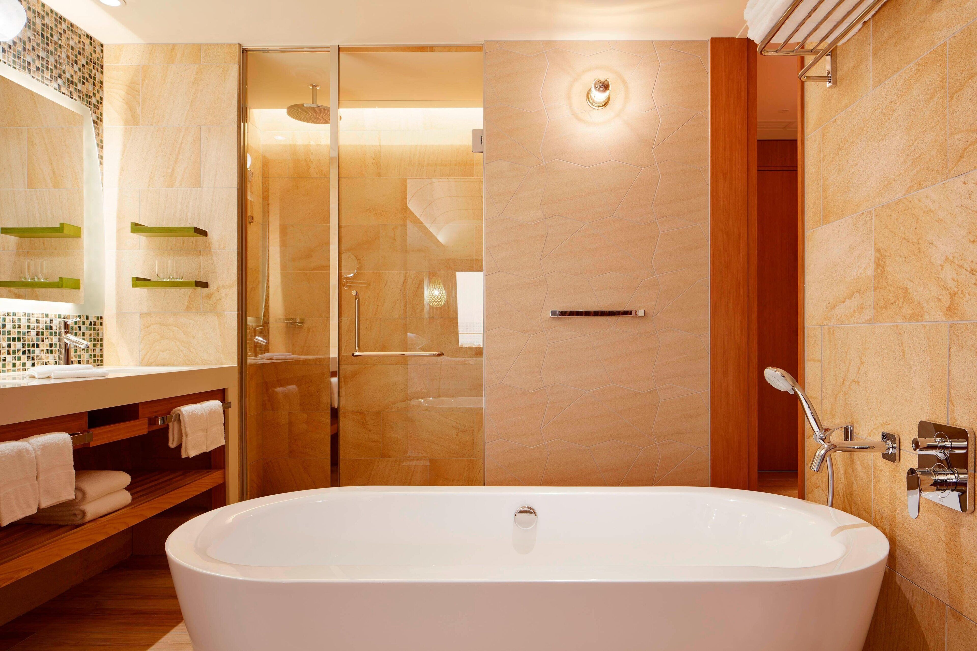 Ein modernes Badezimmer mit freistehender Badewanne, einer Glaskabine zur Dusche und einem Waschtisch mit Spiegel und Handtuchhaltern.
