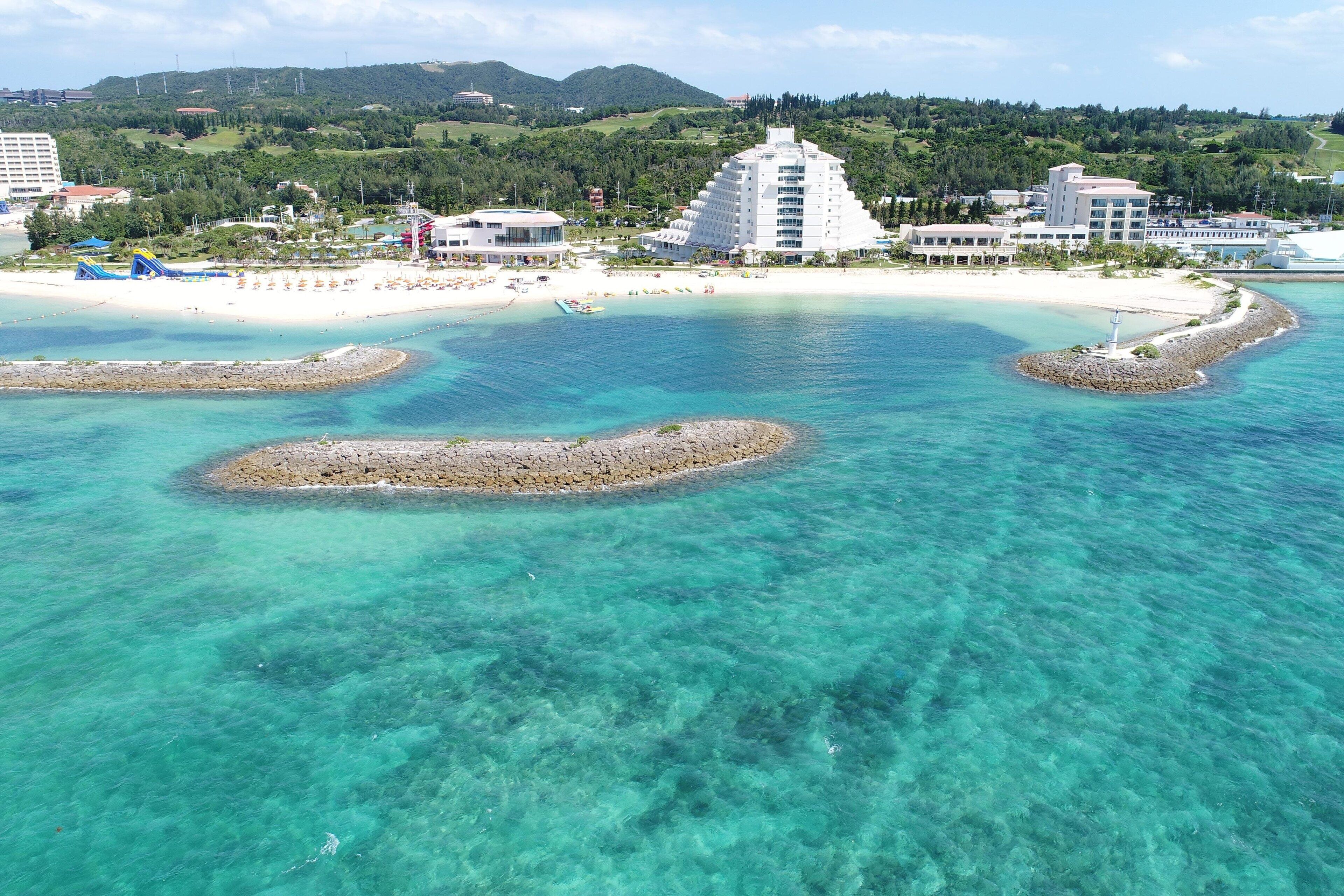 A coastal resort with clear turquoise waters, a sandy beach, and a distinctive white building with multiple balconies.