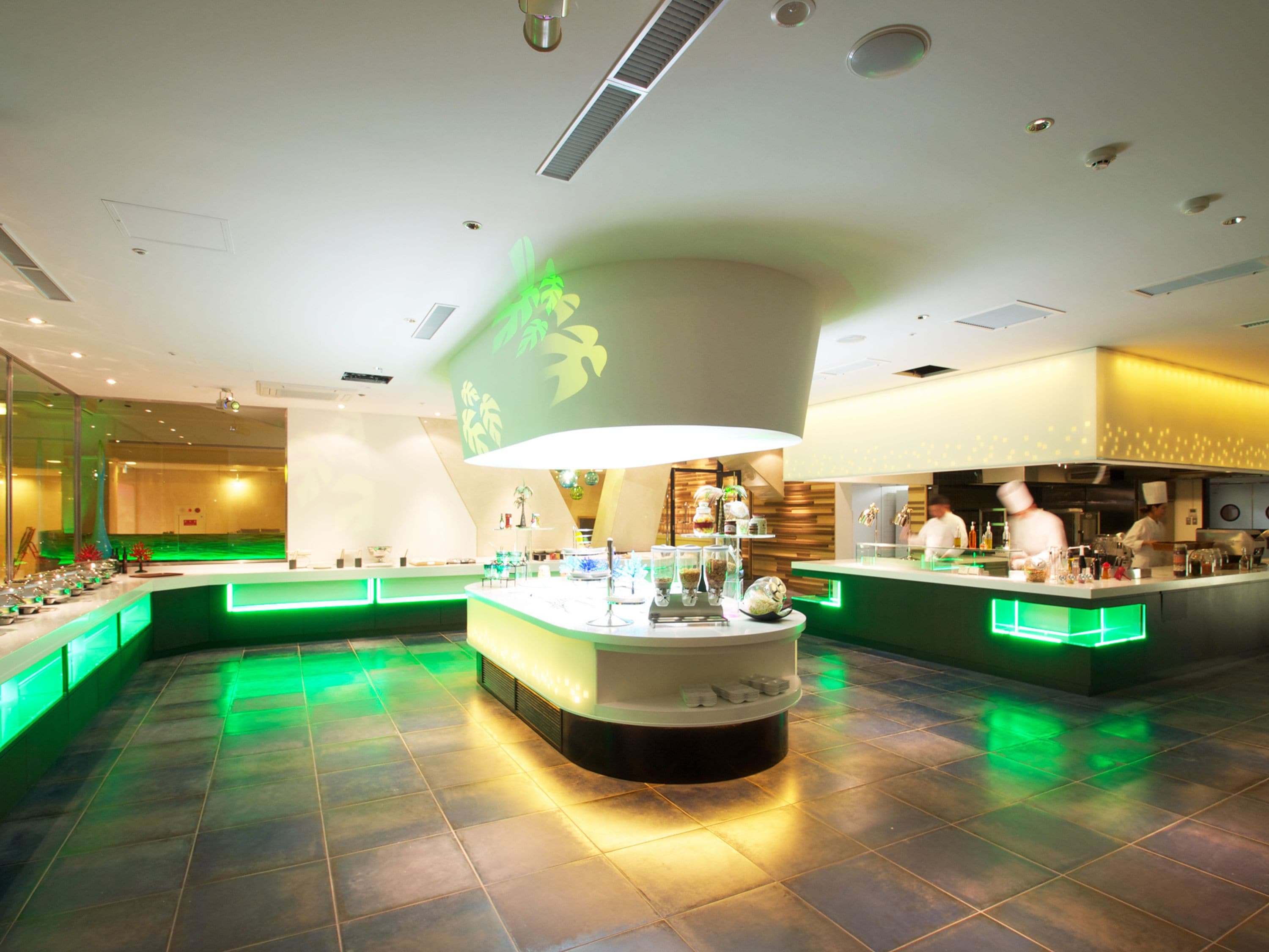 Een modern restaurantinterieur met een centraal eiland, groene sfeerverlichting en een zichtbare keuken in de achtergrond.
