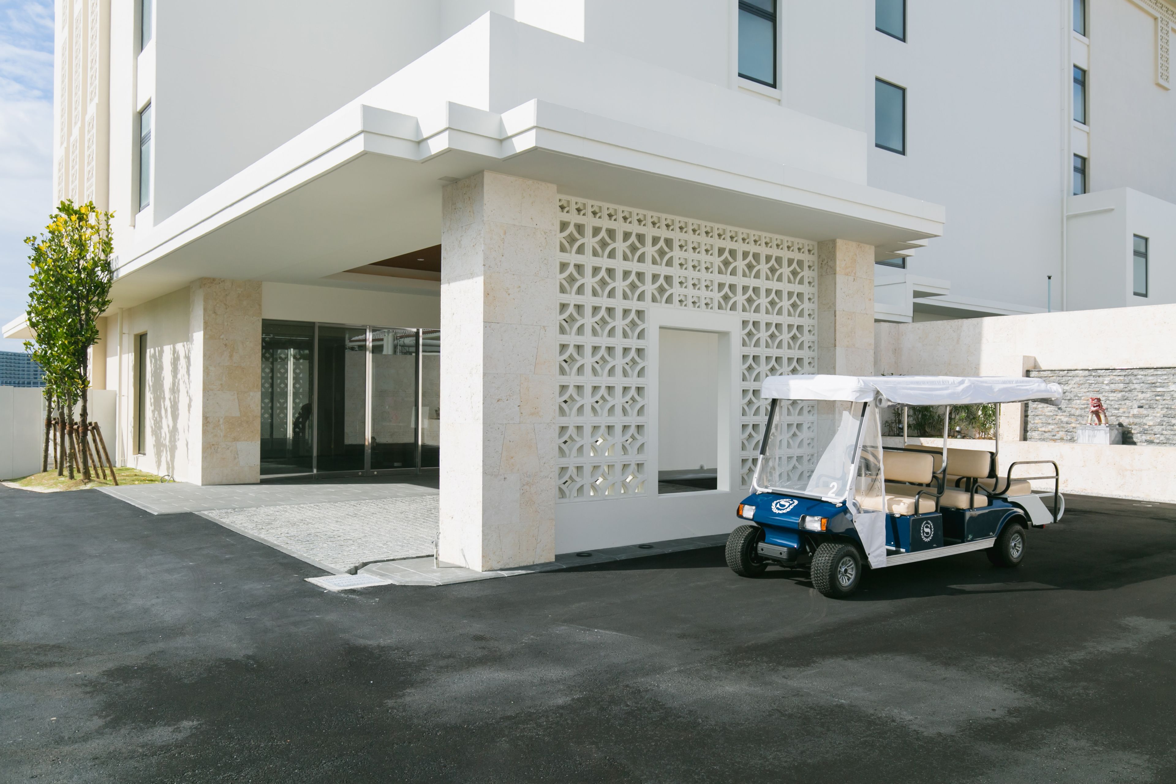 A modern building with a white facade, a covered entrance, and a golf cart parked in front.