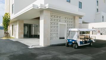 A modern building with a white facade, a covered entrance, and a golf cart parked in front.