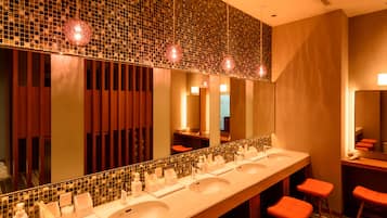 Features a long vanity with three sinks, a large mirror, and a mosaic tile backsplash.