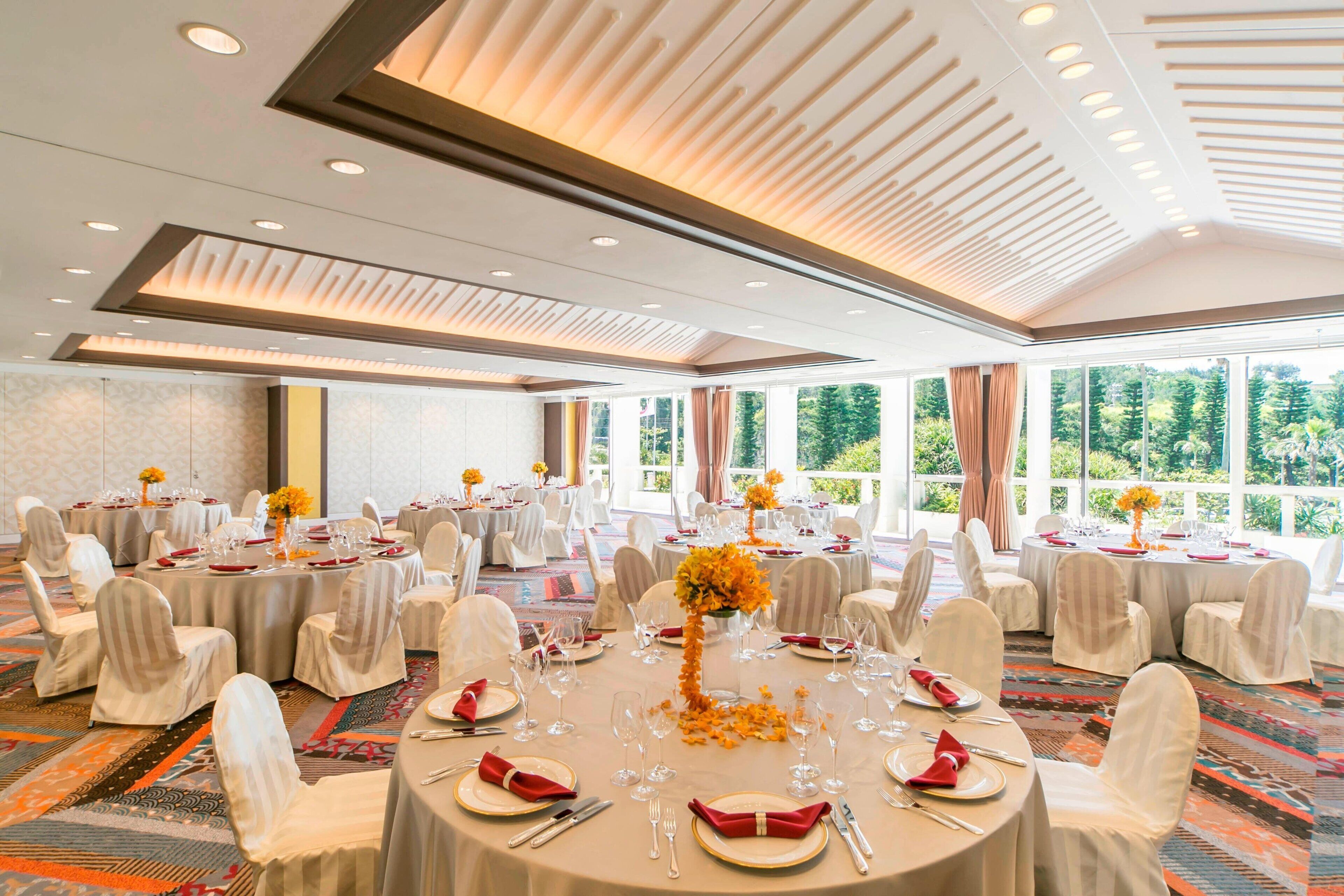 A banquet hall with round tables set for dining, white chairs, and a carpeted floor.