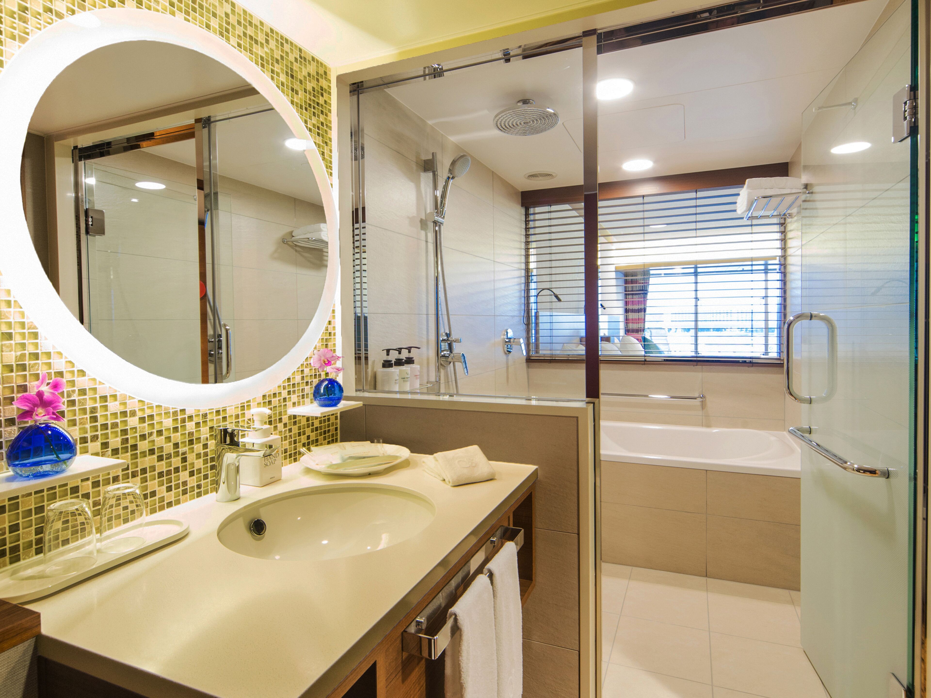 Une salle de bain moderne avec un grand miroir ovale, un lavabo, une douche et une baignoire.