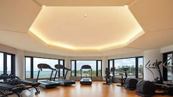 Un gimnasio amplio con diversos equipos de ejercicio, amplias ventanas que ofrecen vistas al océano y un diseño de techo moderno.