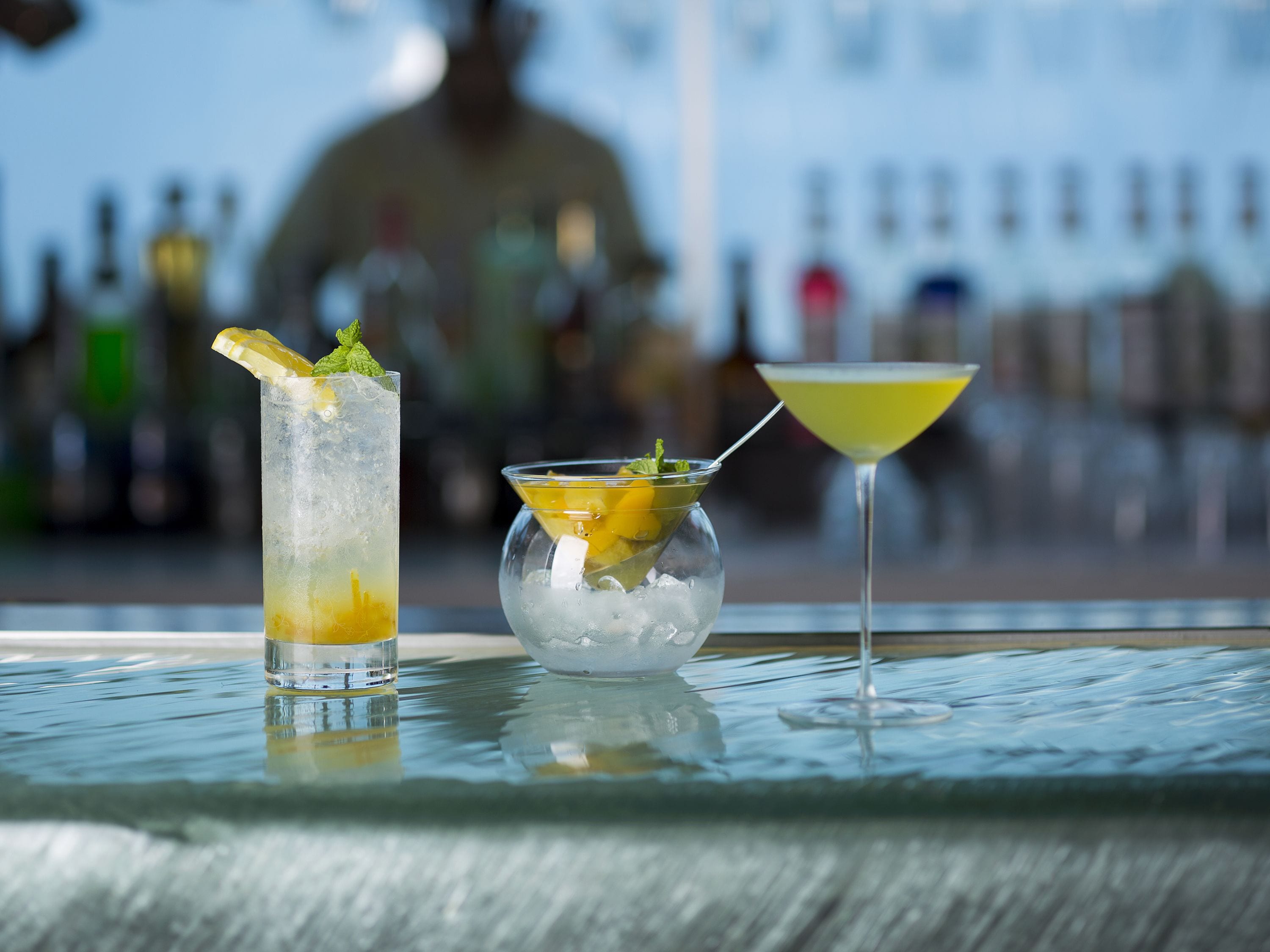 A bar setting with a tall glass and a martini glass on a reflective surface.