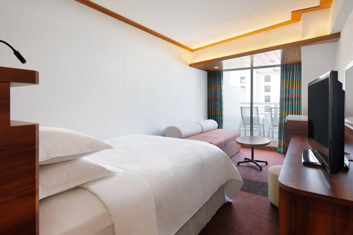 A hotel room with a bed, a desk with a TV, a small table, and a chair.
