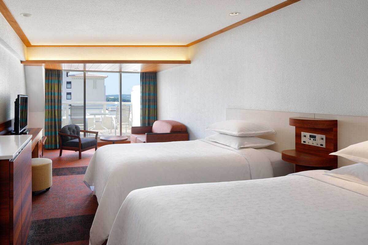 A hotel room with two beds, a desk, a chair, and a TV.