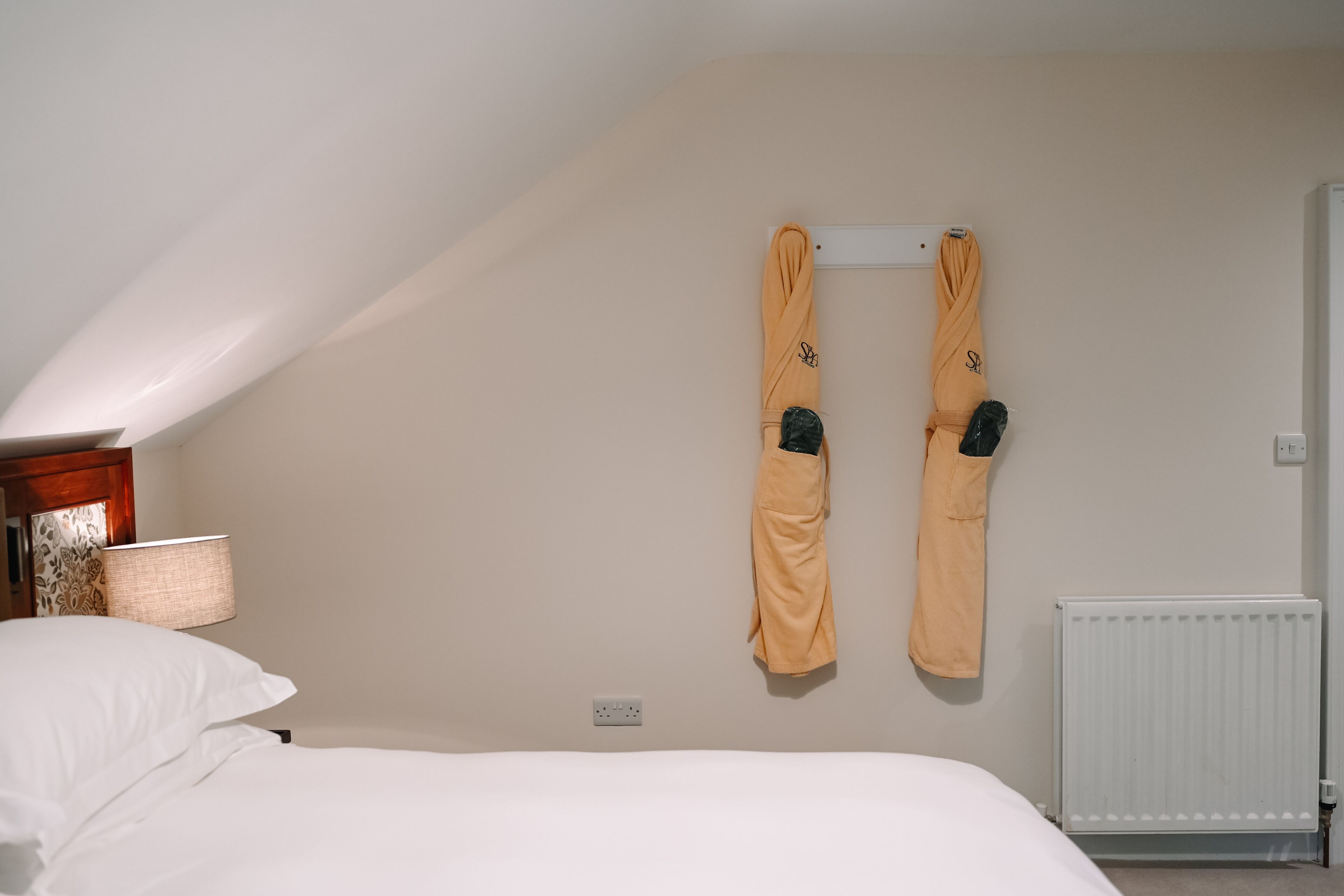 Quarto de hotel com cama, um porta-toalhas fixado na parede com toalhas, luminária e radiador.