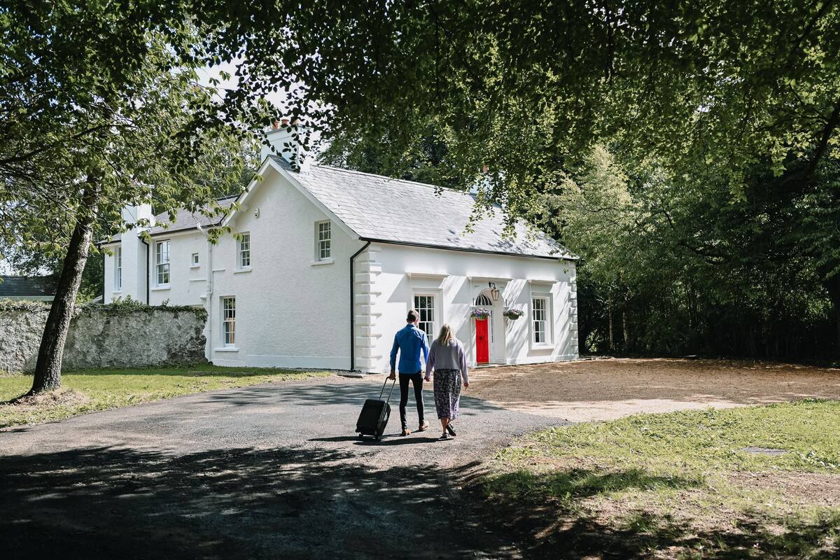 A white building with a red door, a paved driveway, and a grassy area.
