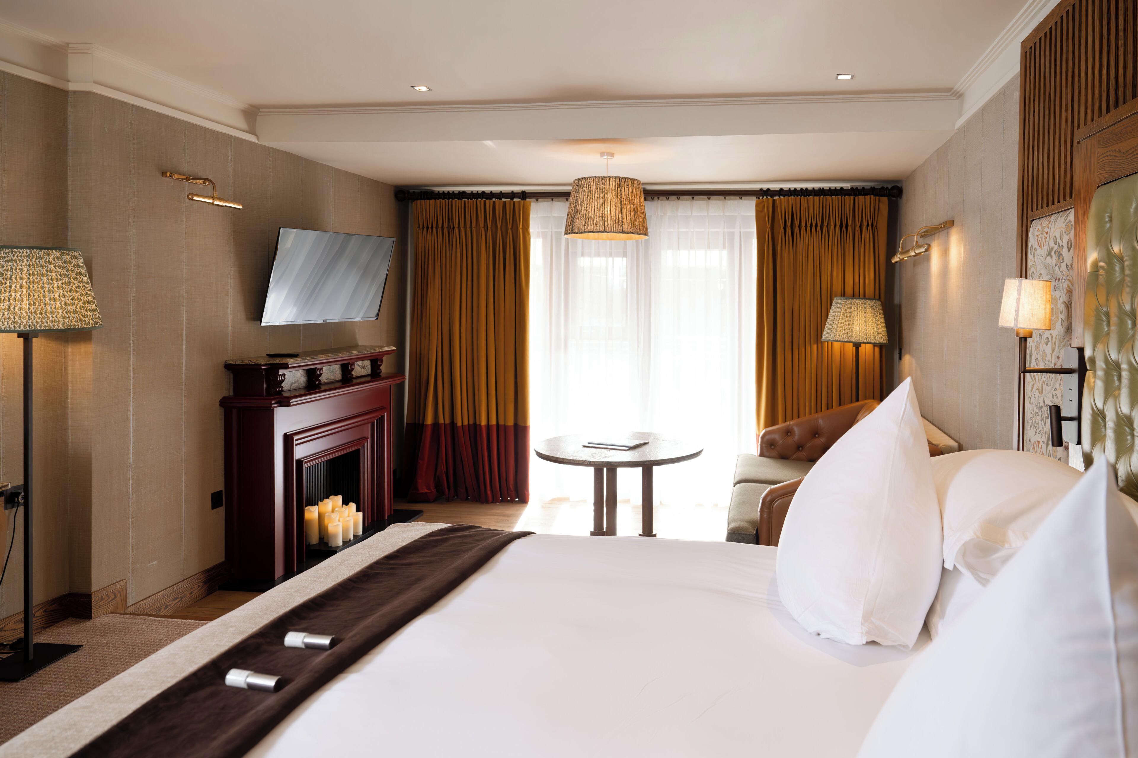 Una habitación de hotel con una cama grande, televisión, chimenea, una mesa redonda y un sofá.