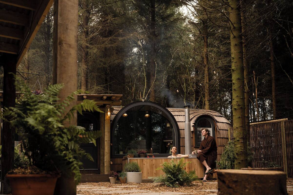 A rustic wooden structure with a large arched window, surrounded by dense forest.