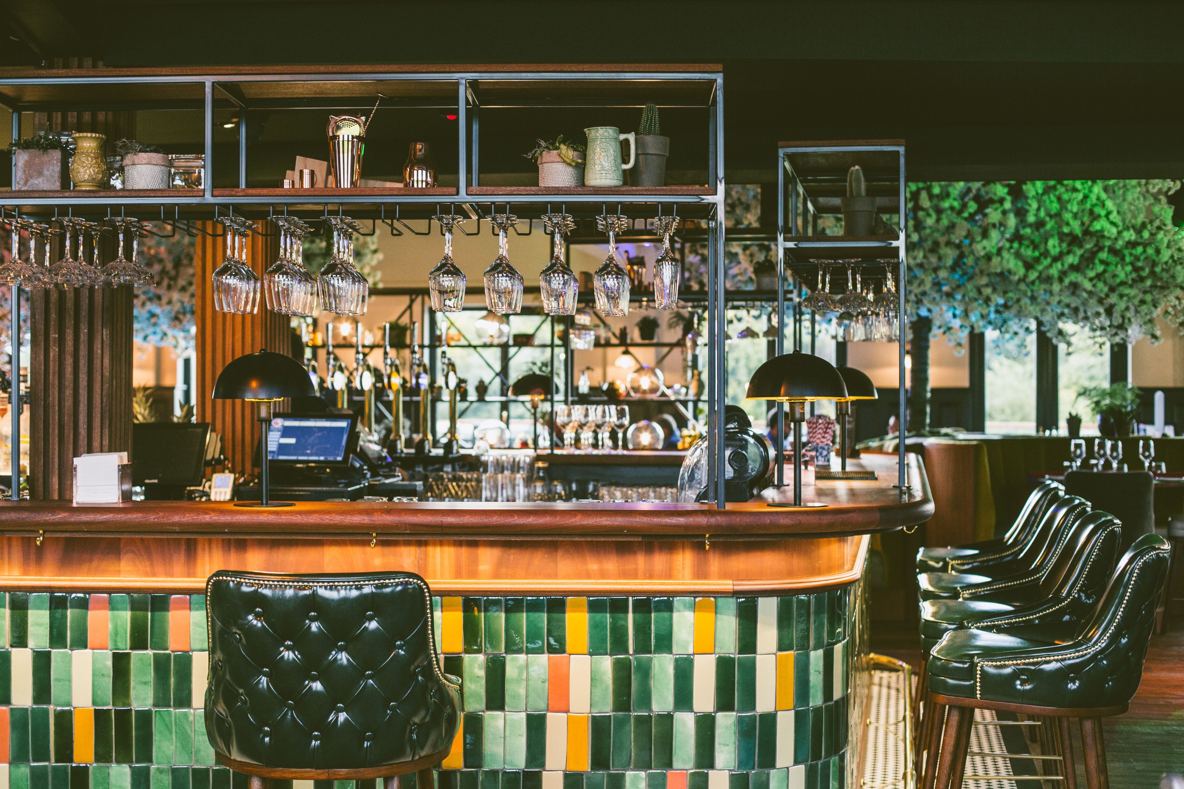Un espace bar agrémenté d’un mur recouvert de carreaux, de verres suspendus et de tabourets de bar en cuir.
