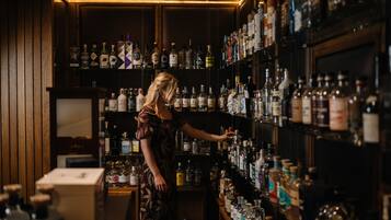 A woman in a dress browsing through a well-stocked liquor shelf in a dimly lit bar.