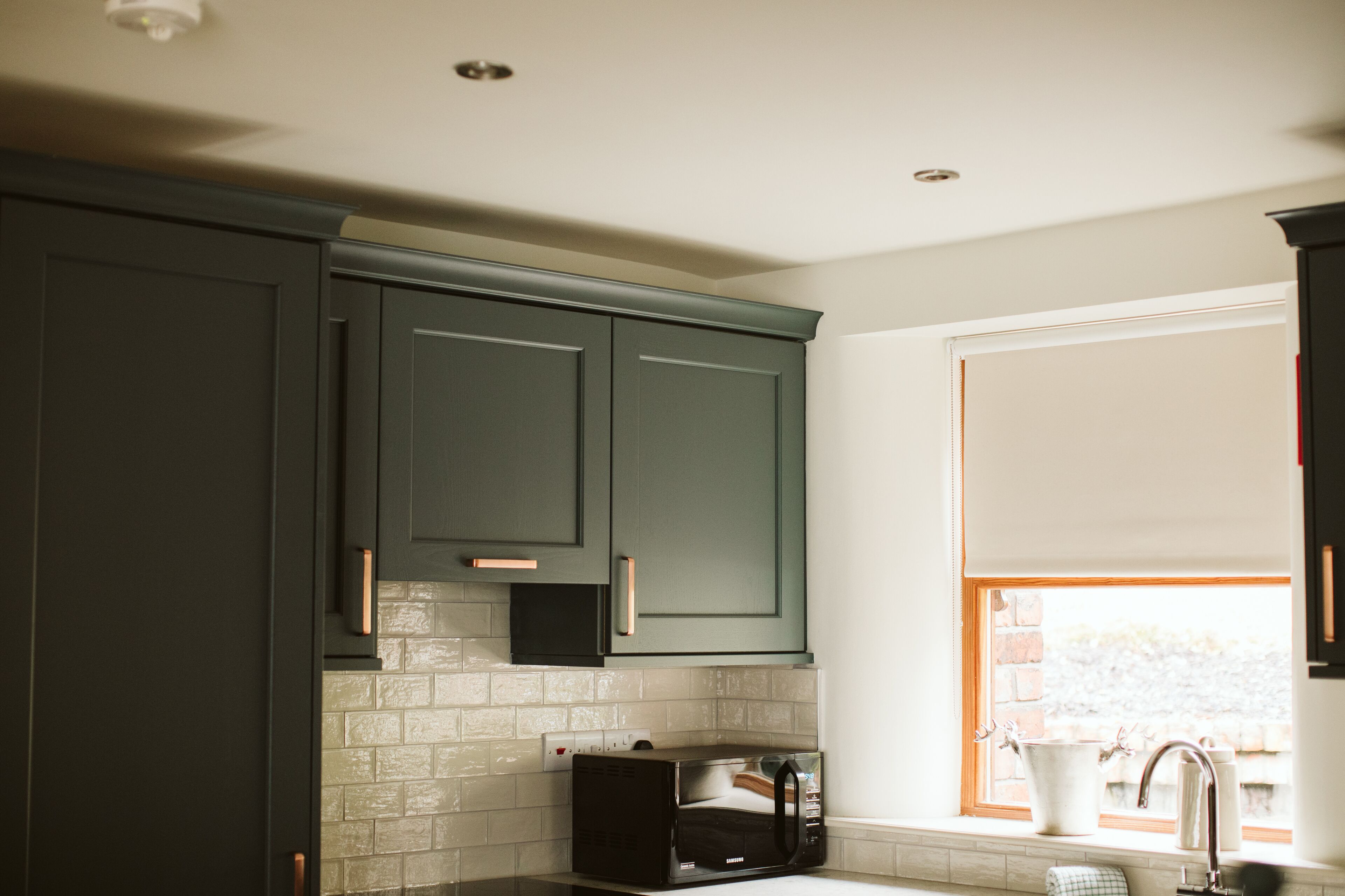 A kitchen with dark green cabinets, a microwave, and a window with a view of a brick wall.