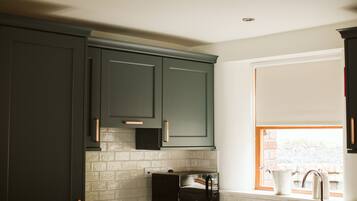 A kitchen with dark green cabinets, a microwave, and a window with a view of a brick wall.