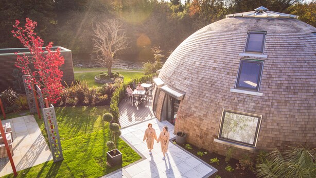 A modern building with a dome-shaped roof, a patio area with seating, and a garden with a tree and shrubs. - Galgorm (Ballymena)