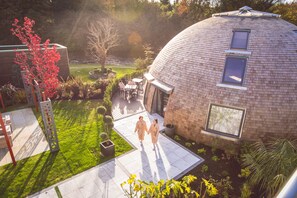 A modern building with a dome-shaped roof, a patio area with seating, and a garden with a tree and shrubs. - Galgorm (Ballymena)