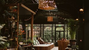 A cozy indoor space with a wooden bench seating area, surrounded by potted plants and a large hanging light fixture. - Galgorm (Ballymena)