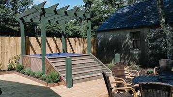 Una terraza de madera con un jacuzzi, sillas de mimbre y una pérgola.