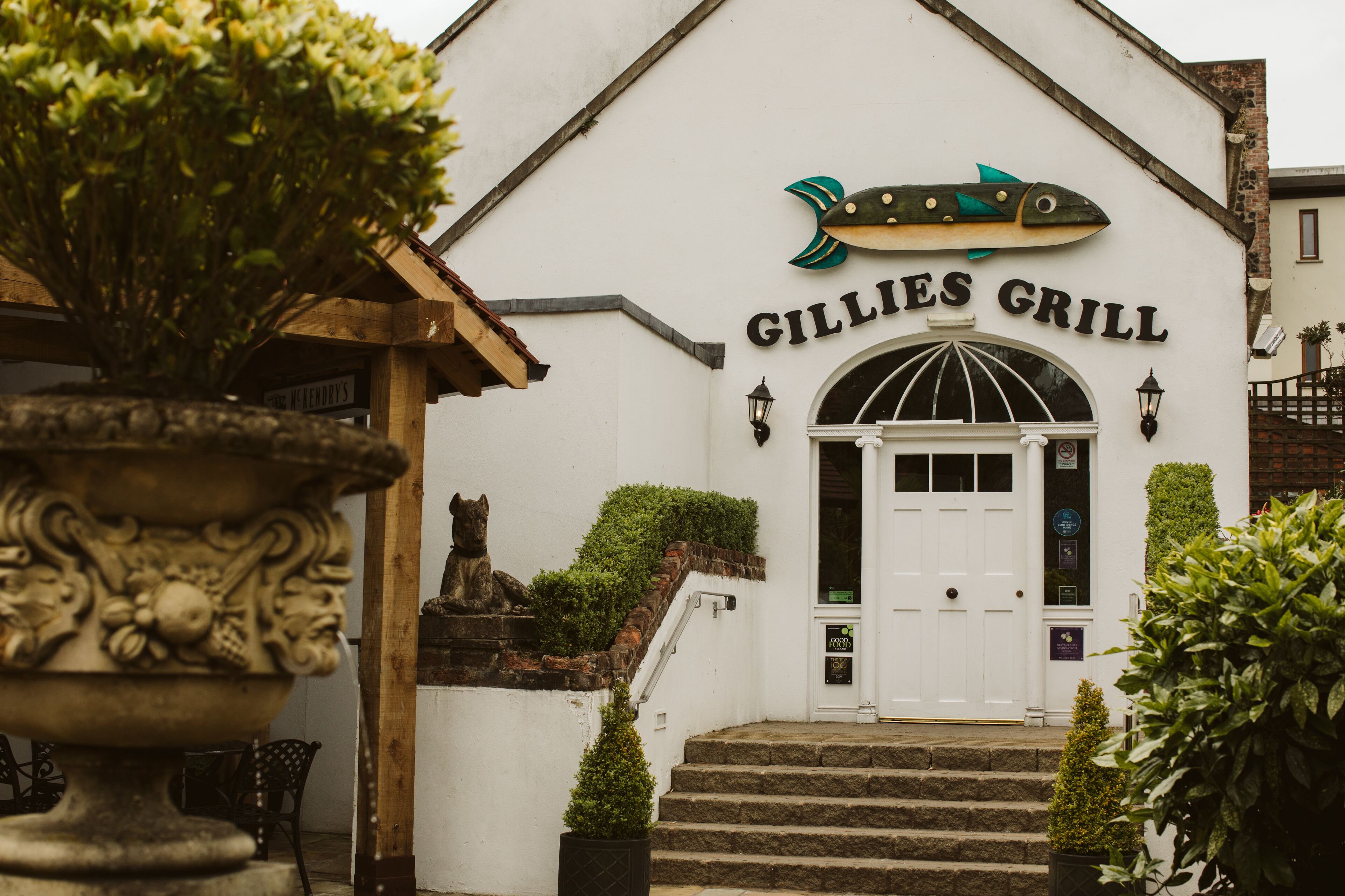 The exterior of Gillies Grill, featuring a fish logo, a white facade, and a set of stairs leading to the entrance.