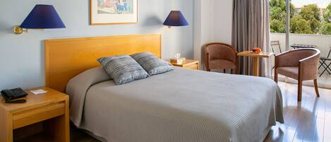 Habitación de hotel con cama, dos lámparas de noche, una mesita con fruta y una silla.