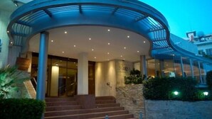 A hotel entrance with a curved glass canopy, a staircase leading to the lobby, and a stone wall with greenery. - Cleopatra Hotel (Nicosia)