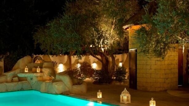 A nighttime pool area with a stone wall, trees, and lanterns. - Cleopatra Hotel (Nicosia)