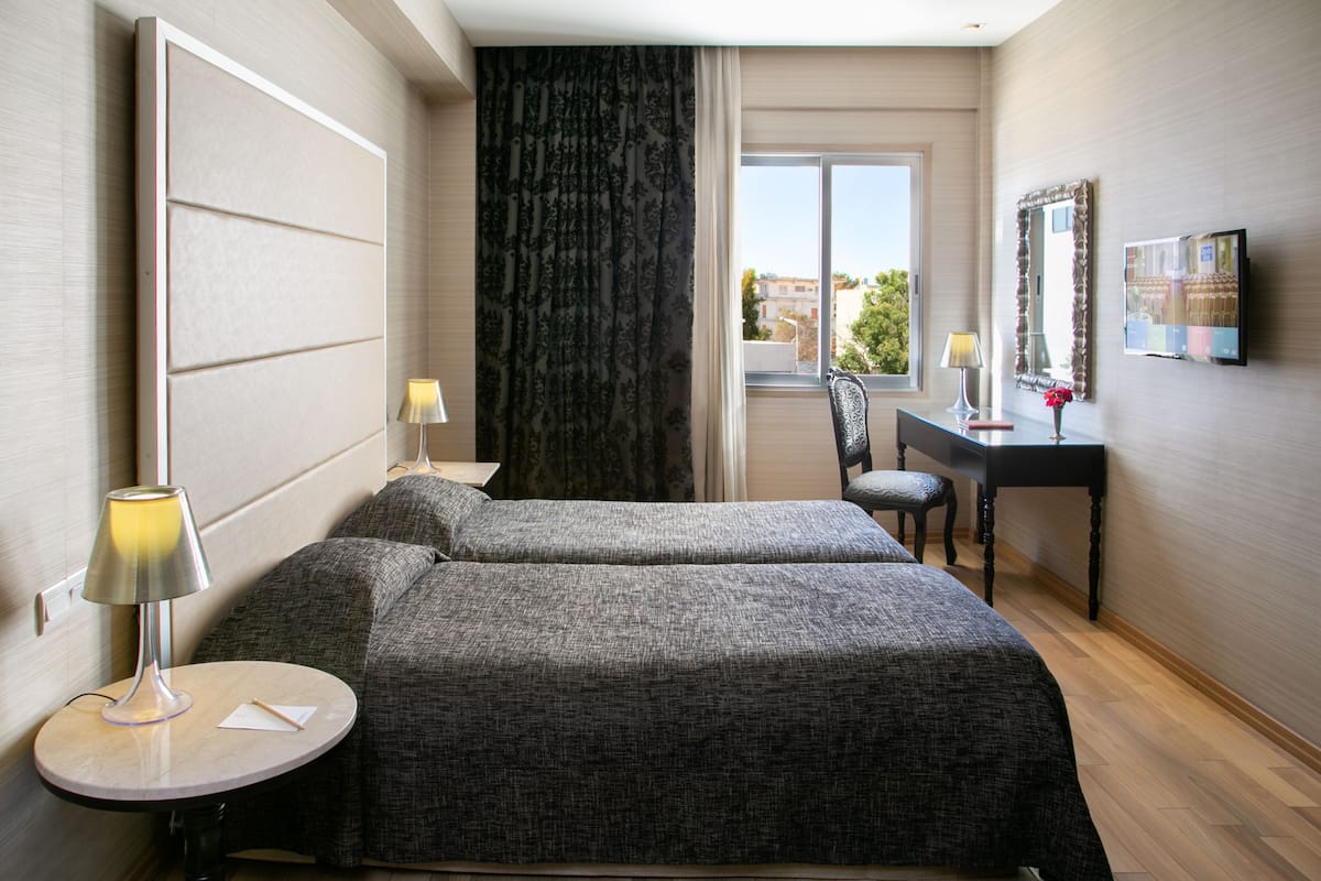 Habitación de hotel con dos camas, un escritorio, una silla, un televisor y una ventana con vistas.