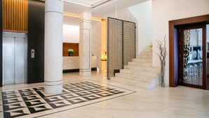 A modern hotel lobby with a marble staircase, a patterned floor, and a reception area with a wooden panel and a vase of flowers. - Cleopatra Hotel (Nicosia)