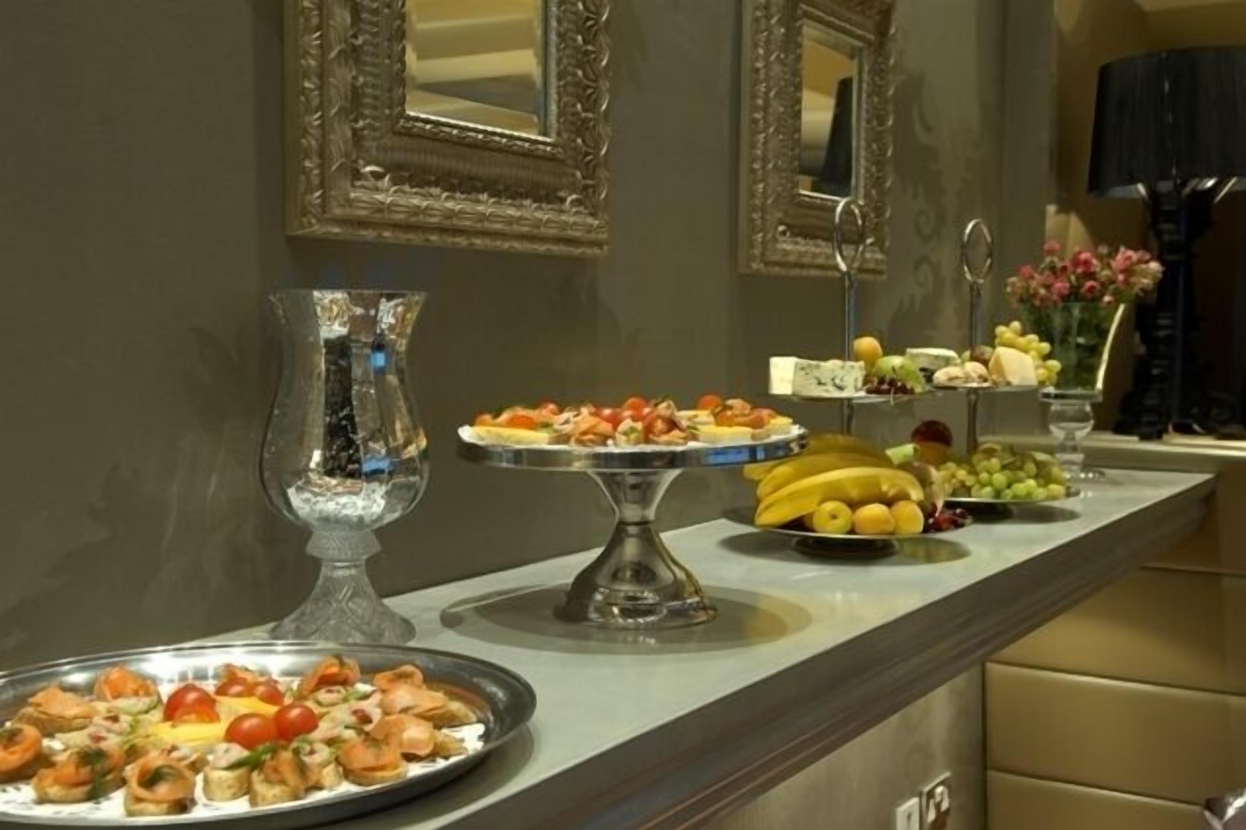 A buffet table with various food items, including fruits and appetizers, in a room with mirrors and a vase of flowers.