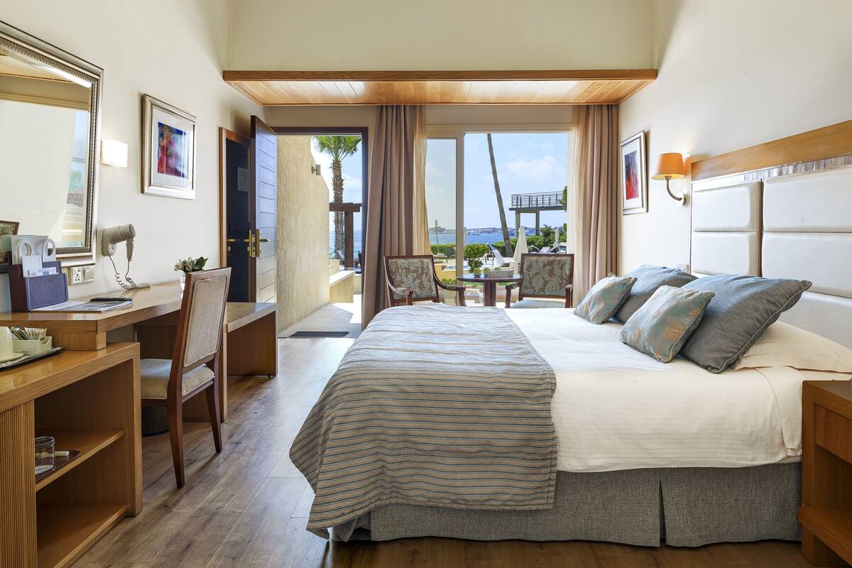 A hotel room with a bed, desk, chair, and a view of the sea.