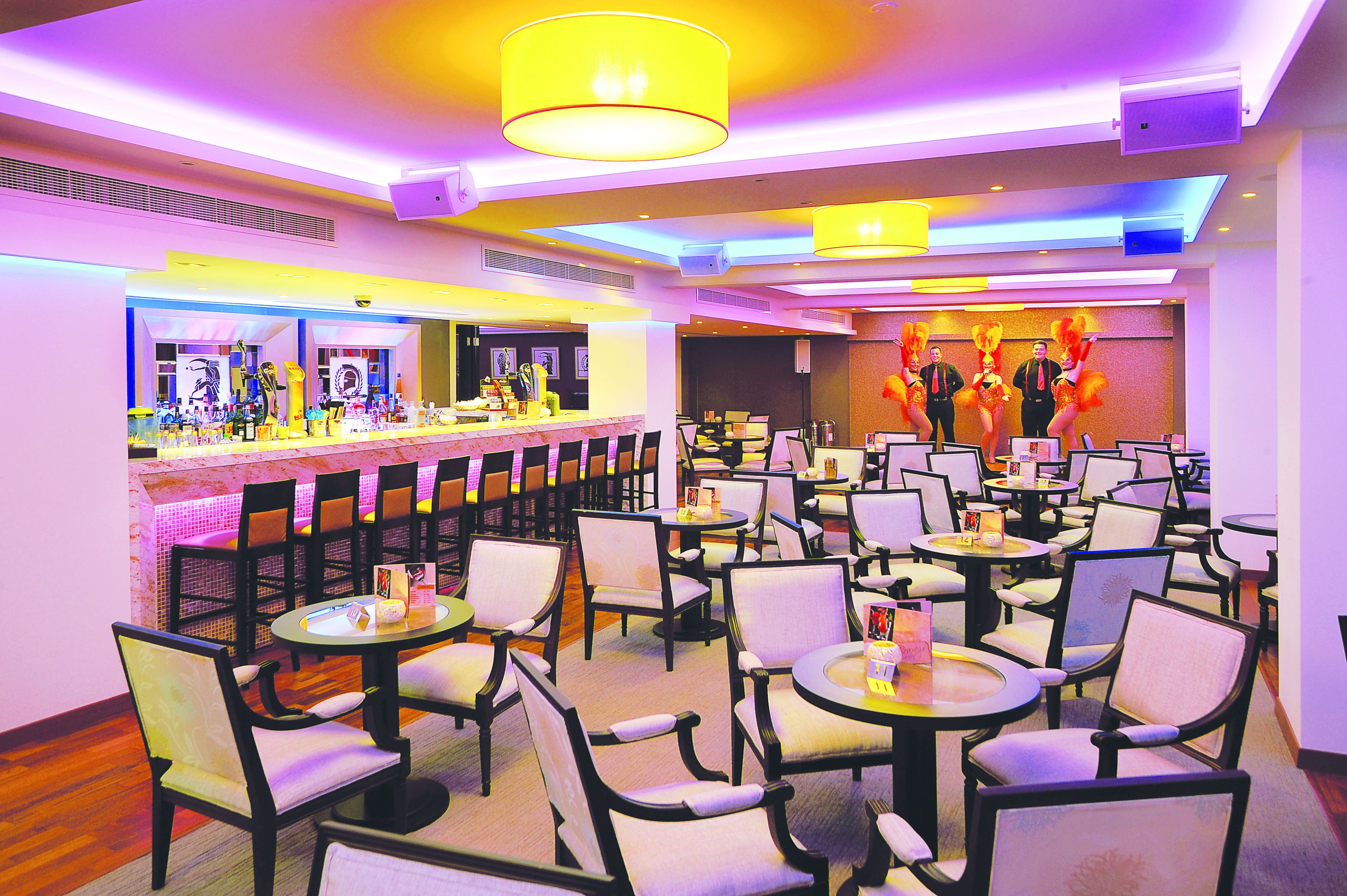 A restaurant with multiple tables and chairs, a bar area, and a stage with performers.
