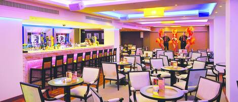 A restaurant with multiple tables and chairs, a bar area, and a stage with performers.