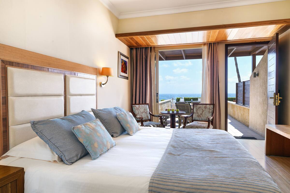 A hotel room with a bed, a table with chairs, and a view of the sea.