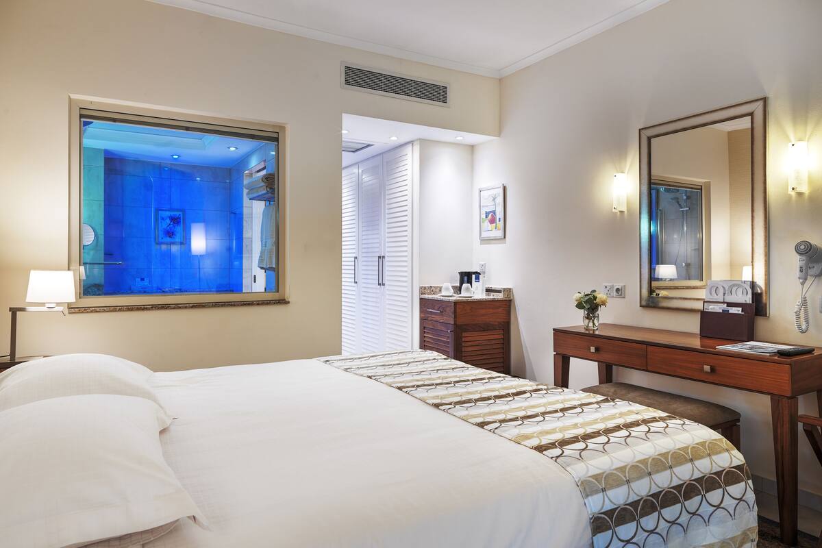 A hotel room with a large bed, a dresser with a mirror, a hairdryer, and a view of the bathroom.