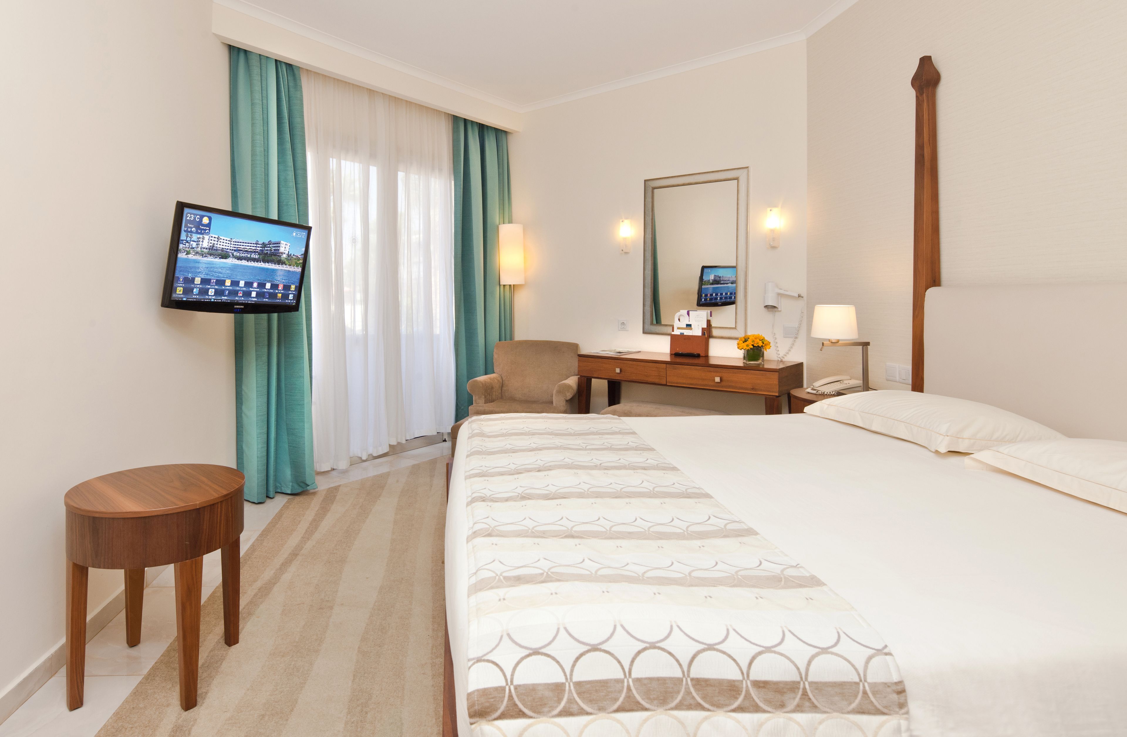 A hotel room with a bed, a desk, a chair, a TV, and a window with curtains.