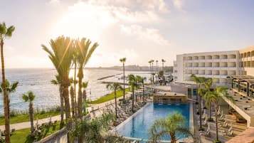 Relax by the infinity pool overlooking the ocean, surrounded by palm trees and lounge chairs.