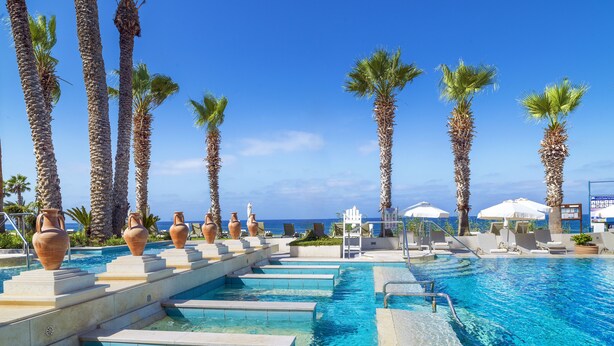 Un espace piscine avec une eau d’un bleu limpide, entouré de palmiers et de grands vases.