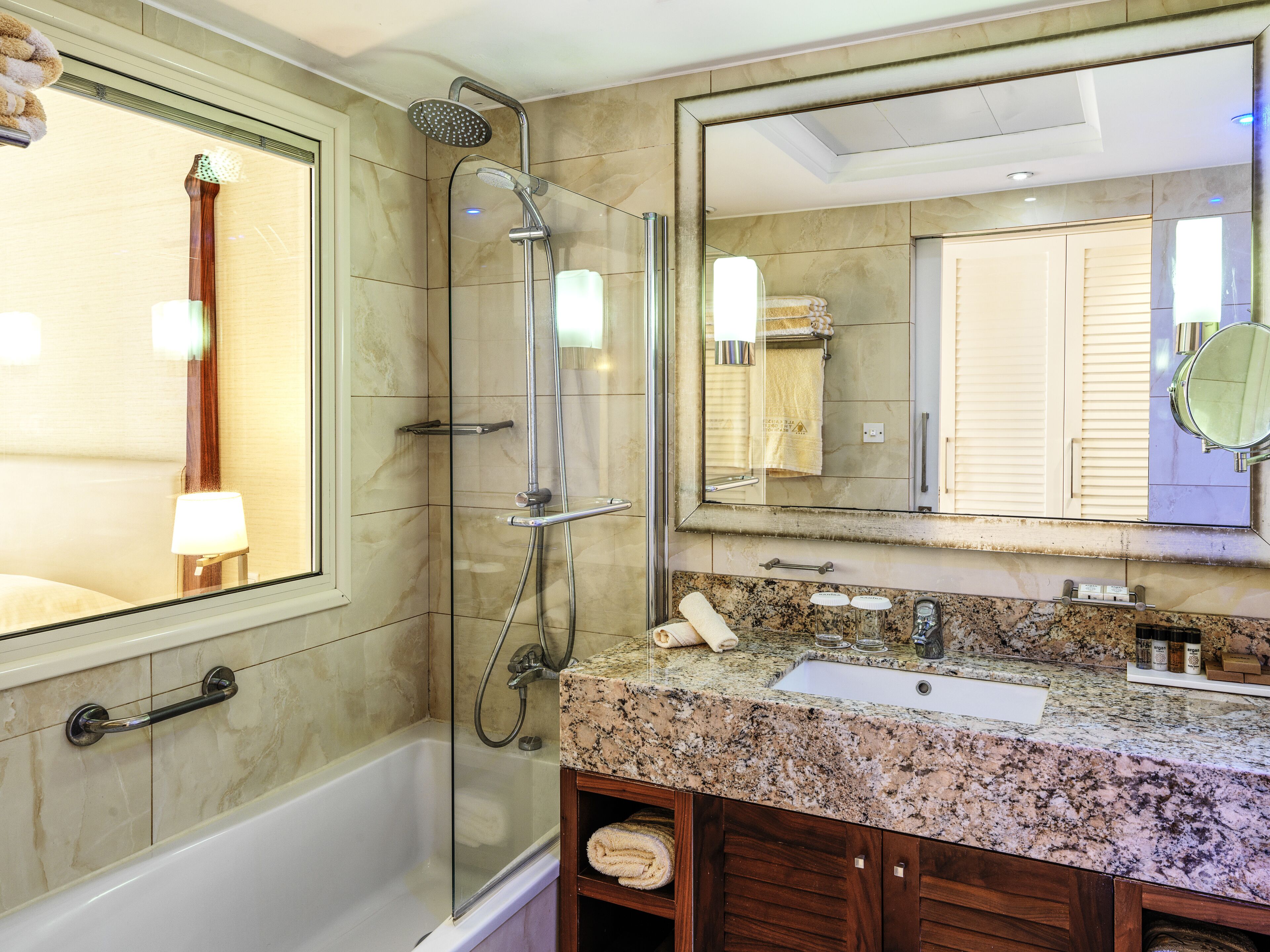 A modern bathroom with a glass-enclosed shower, a bathtub, a granite countertop, a sink, and a large mirror.