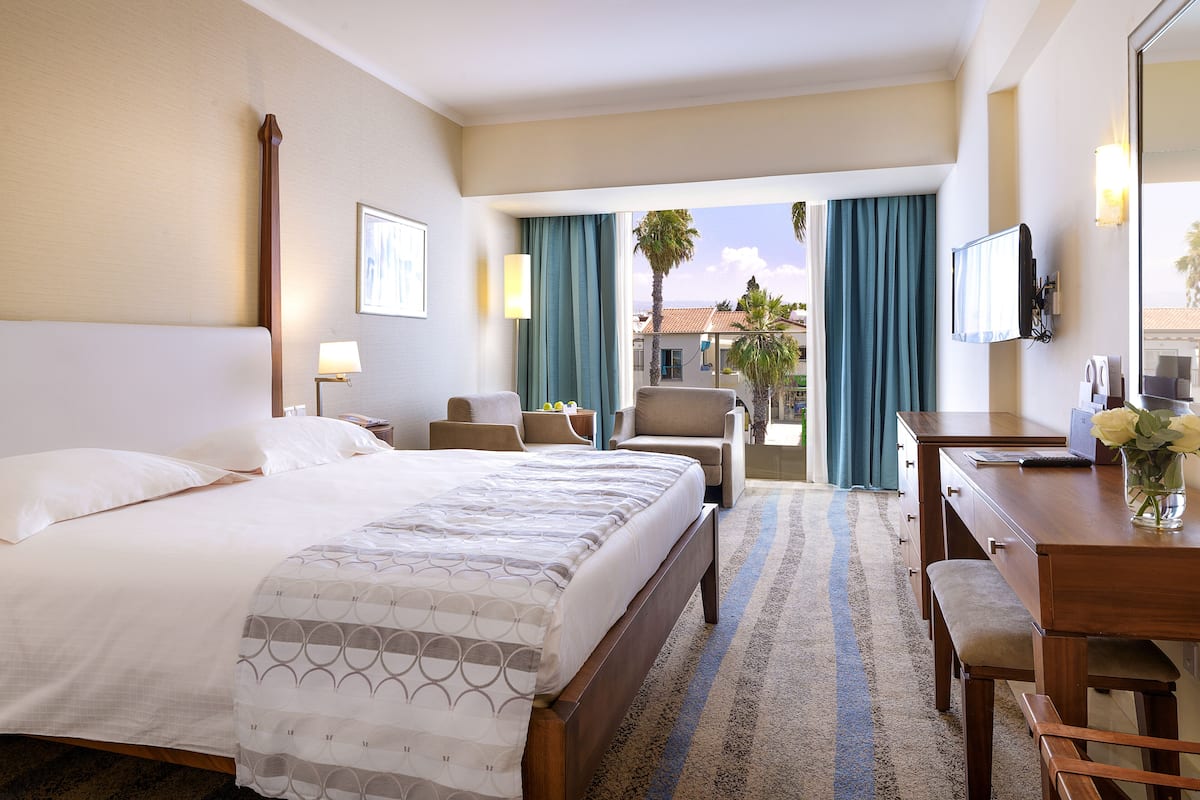 Ein Hotelzimmer mit Bett, Schreibtisch, Stuhl, Fernseher und Blick ins Freie.