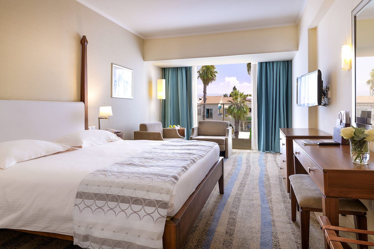 A hotel room with a bed, a desk, a chair, a TV, and a view of the outside.