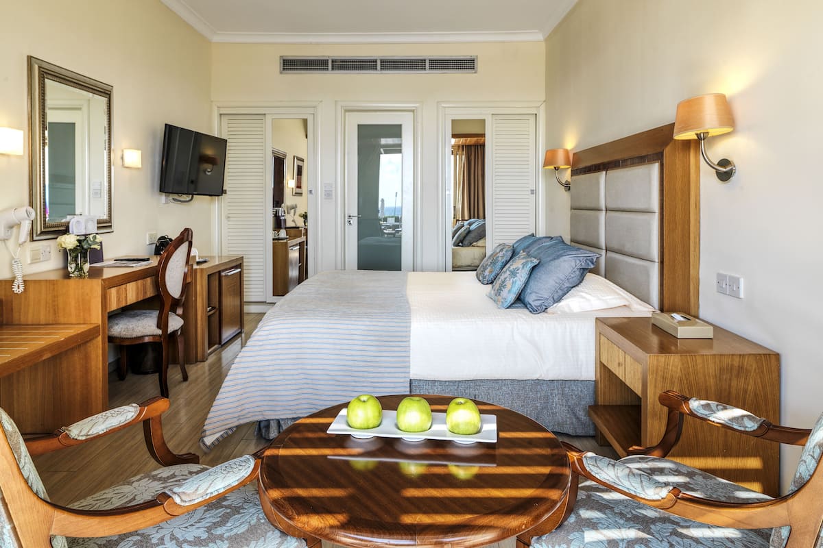 A hotel room with a bed, a desk, a chair, a table with apples, and a TV.