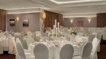 A banquet hall with round tables, white chairs, and floral centerpieces.