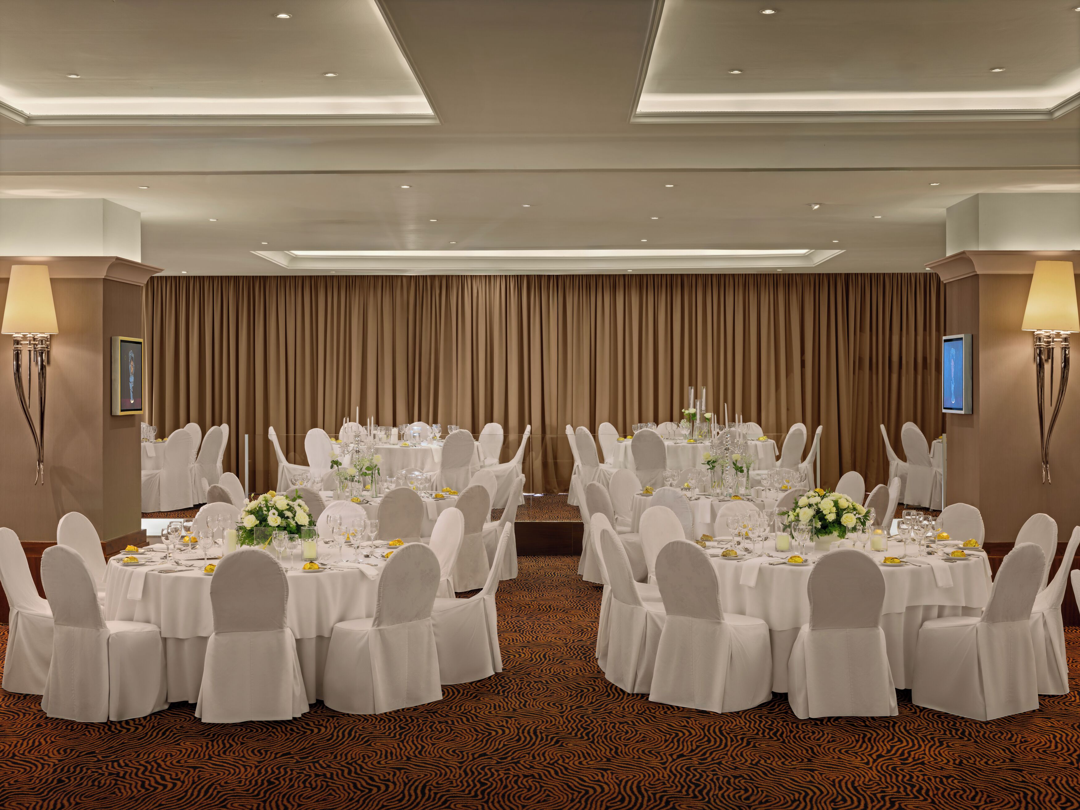 Une salle de banquet avec des tables rondes, des chaises blanches et des centres de table floraux.