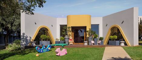 A modern building with a yellow central section, arched doorways, and a well-maintained lawn with outdoor seating.