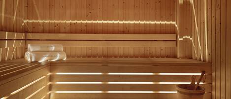 A sauna with wooden benches and benches, a wooden bucket with a wooden mallet, and a towel labeled 'Mediterranean' on the bench.