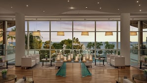 Eine großzügige Lobby mit Meerblick, ausgestattet mit einer Sitzecke, Tischen, einer Treppe und großen Fenstern.
