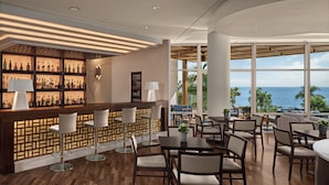 Eine Bar mit Holztresen, Barhocker und Blick auf das Meer.