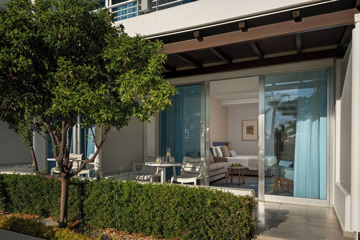 Una habitación de hotel moderna con puerta de vidrio, sofá, una mesita y ventana con vistas.